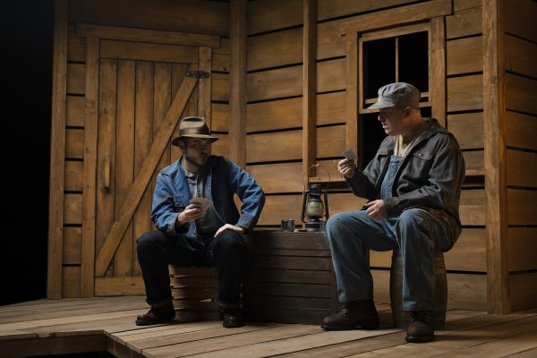 Two men as Lennie and George onstage, playing cards 